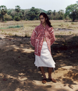 Model Theia Maeve standing outdoors in a textured red jacket and white skirt for the Maatii Studio campaign. 
