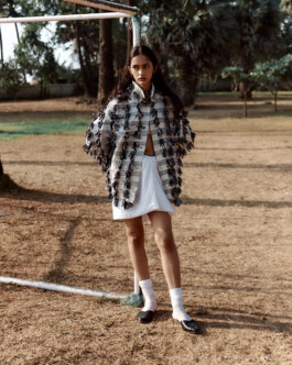 Model Theia Maeve standing outdoors in a textured handcrafted jacket and white skirt for the Maatii Studio campaign. 